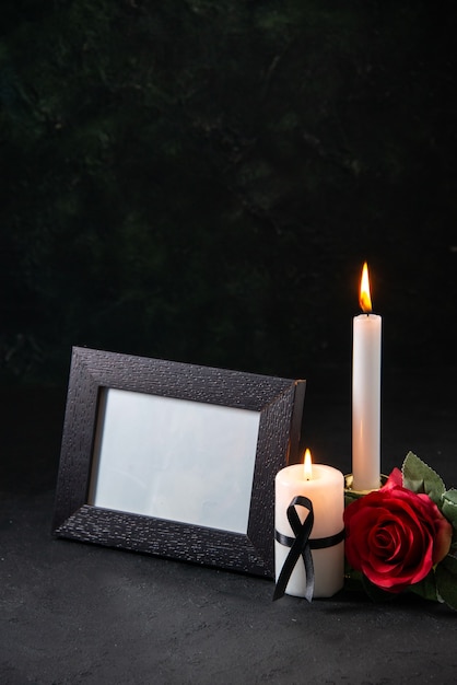 Front view of burning candles with red flower on dark surface