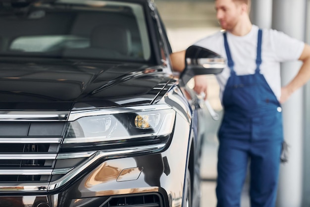 Front view of the car Young man in white shirt and blue uniform repairs automobile