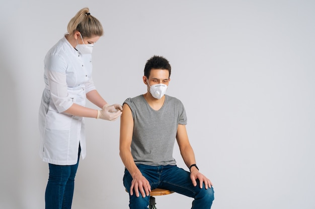 Front view of Caucasian male in face mask receiving vaccine against coronavirus on isolated background. Portrait of doctor using syringe to inject vaccine to patient prevent spread of virus covid19.