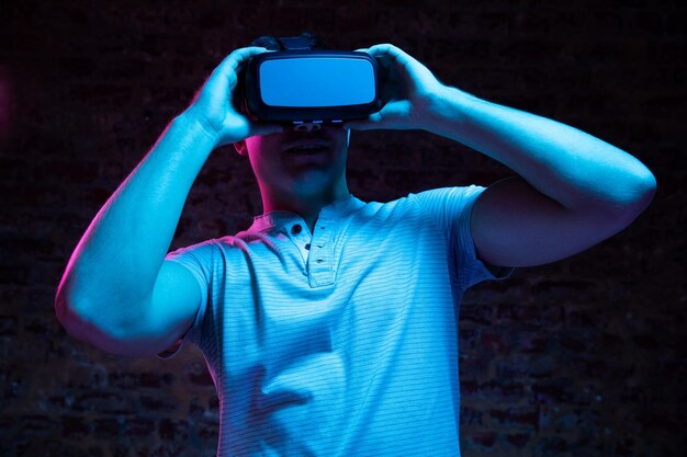 Front view of a Caucasian man wearing a Virtual Reality headset and looking around, lit with pink and blue light on a black background.