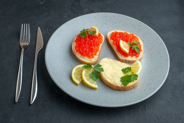 front view caviar sandwiches with lemon and cutlery inside blue plate on dark surface