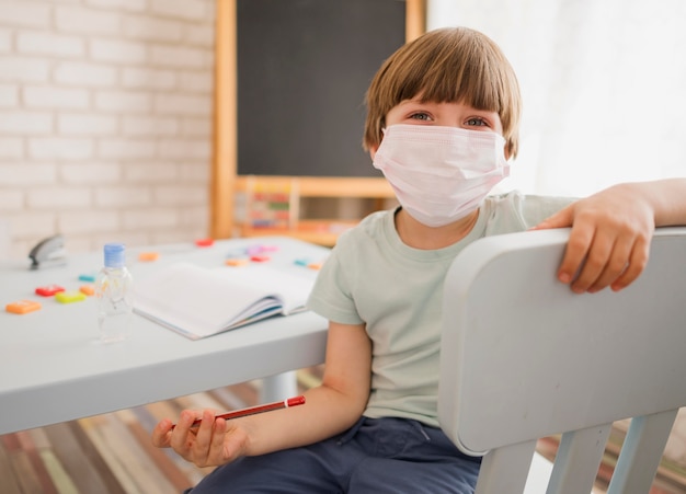 Front view of child being tutored at home while wearing medical mask