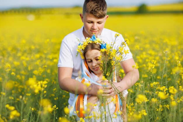 Front view of children brother and sister walking far away along path with grass surrounded by yellow fields