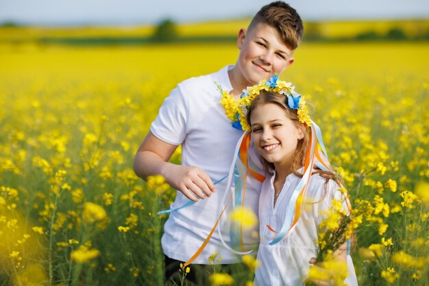 Front view of children brother and sister walking far away along path with grass surrounded by yellow fields