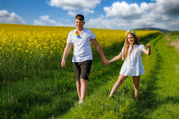 Front view of children brother and sister walking far away along path with grass surrounded by yellow fields