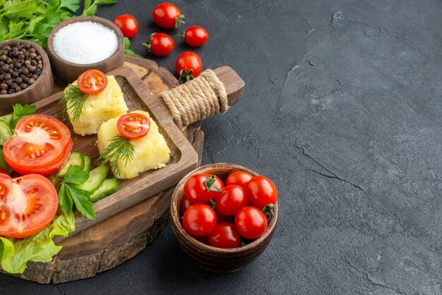 Front view of chopped fresh vegetables cheese on cutting board and spices green bundle on the right side on black surface