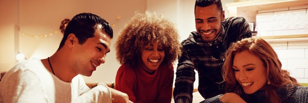 Front view close up of a group of young adult multi-ethnic male\
and female friends socialising sitting in the kitchen of an\
apartment, looking at a smartphone and laughing together