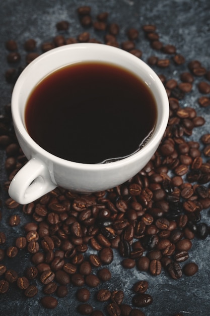 Front view of coffee seeds with cup of coffee on dark surface