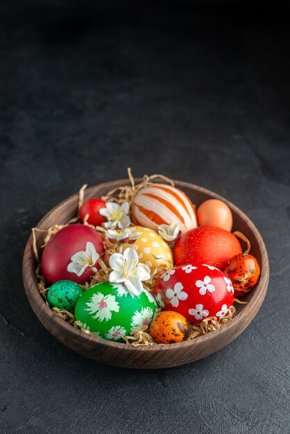 front view colored easter eggs inside brown plate on dark surface