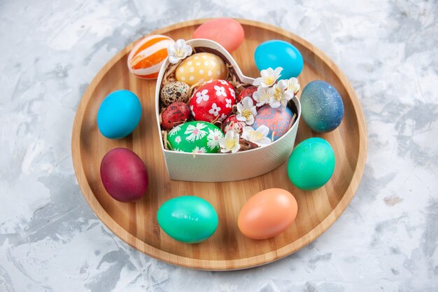 front view colored easter eggs inside heart shaped box and on cutting board white surface holiday concept easter spring ornate