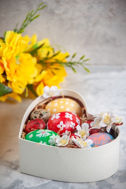 front view colored easter eggs inside heart shaped box with yellow flowers white surface holiday concept easter spring ornate colourful