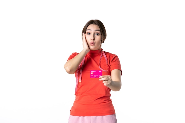 Front view of a confused young girl in redorange blouse showing bank card on white background