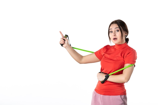 Front view of a curious young woman neatly gathering her hair dressed in redorange blouse and holding rope sport accessory pointing up on white background