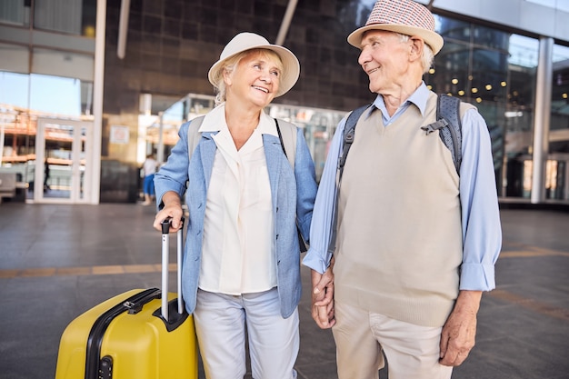 Front view of a cute happy senior tourist gazing with love at her pleased husband