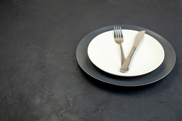 Front view of cutlery set on dark color and white empty plates in different sizes on black background