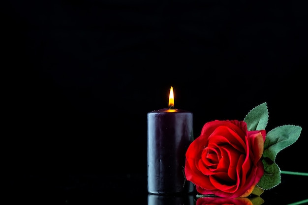 Front view of dark candle with red rose on the dark surface