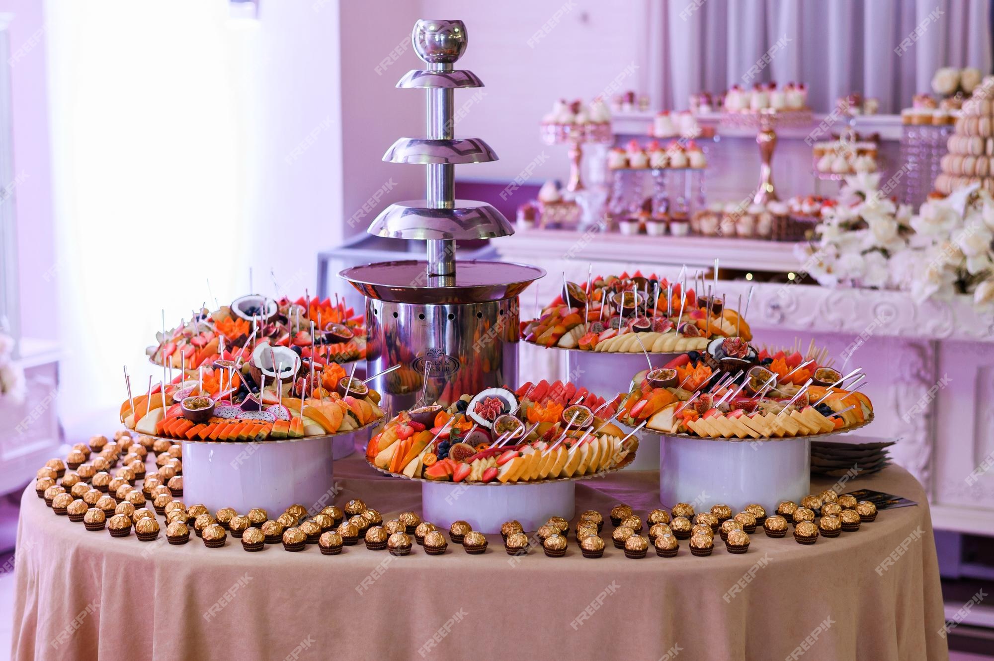 Premium Photo | Front view of decorated table with chocolate fountain  plates with fresh sliced tropical fruits and sweets which placed on  background of candy bar during wedding party in luxury restaurant