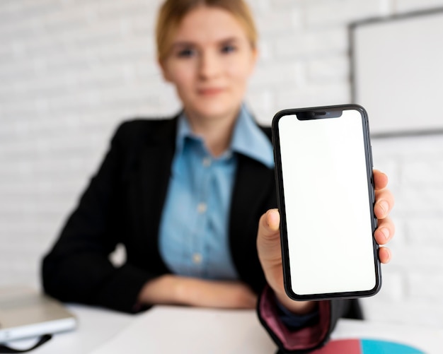 Foto vista frontale della donna di affari defocused che tiene smartphone in ufficio