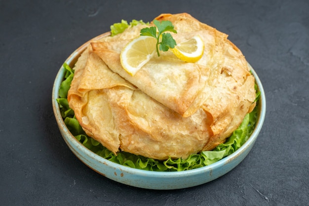 Front view delicious cooked pita inside plate with greens and lemon on dark surface