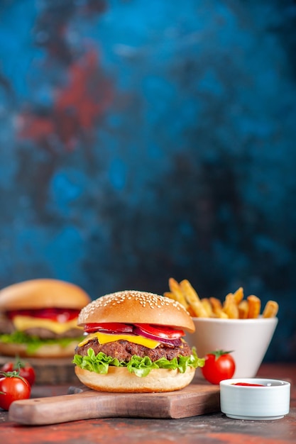 Vista frontale deliziosi cheeseburger di carne con pomodori e patatine fritte al buio