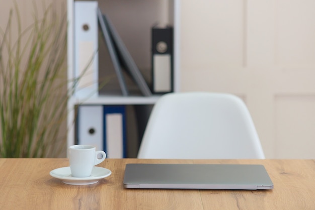 Front view of desktop with closed laptop computer, cup of coffee and office plants