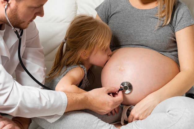 Photo front view doctor listening pregnant mother belly