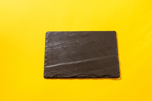 Front view of empty slate black stone plate on the yellow background