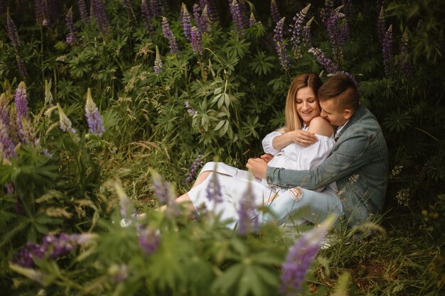 Front view of expecting child couple sitting on grass in lupine meadow