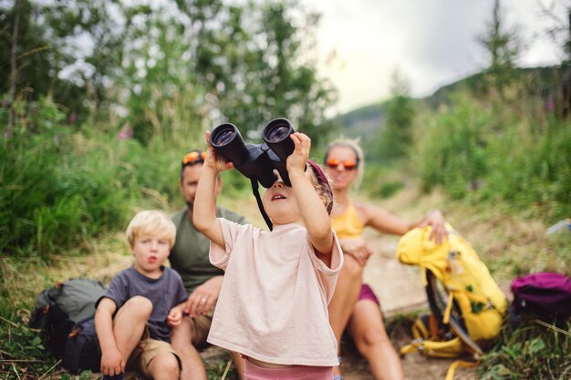 Photo front view of family with small children hiking outdoors in summer nature, sitting and resting.