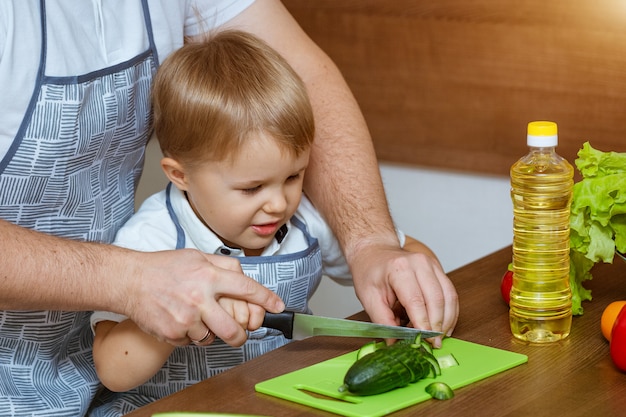 Il padre ed il figlio di vista frontale in cucina hanno tagliato le verdure per insalata.