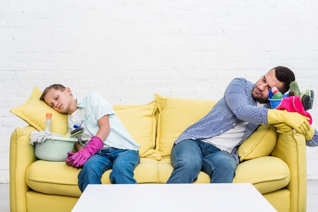 Photo front view of father and son resting on sofa after cleaning