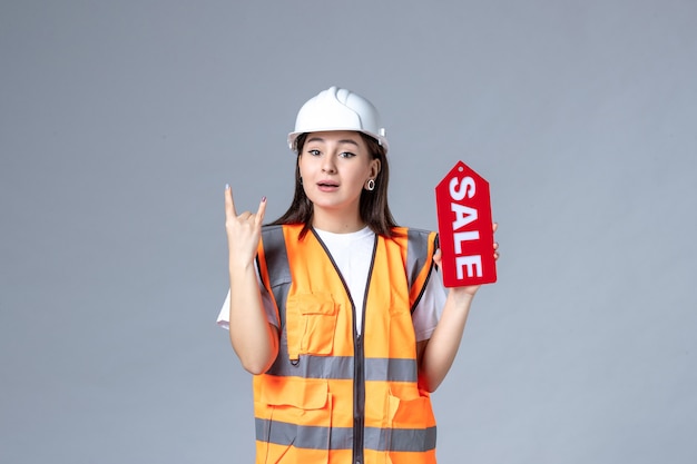 Front view of female builder holding red sale board on gray wall