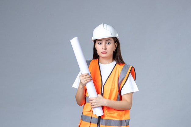 Front view of female builder in uniform with poster in her hands on white wall