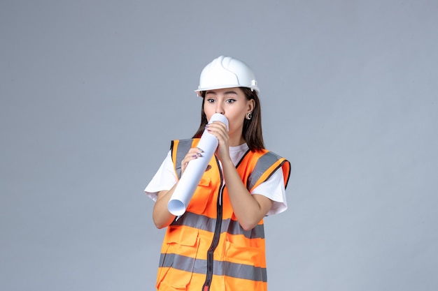 Front view of female builder in uniform with poster in her hands on white wall