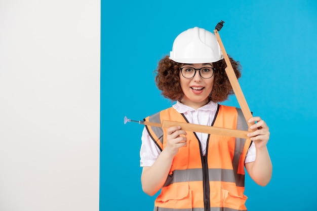 Foto costruttore femminile di vista frontale in uniforme con strumento di legno sull'azzurro