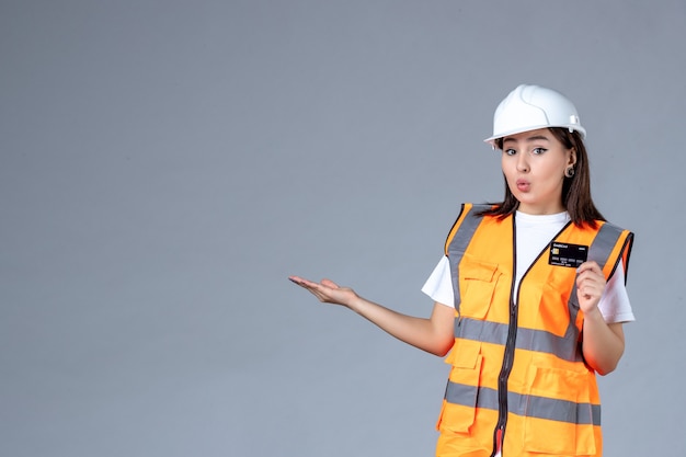 Front view of female builder with black bank card in her hands on gray wall