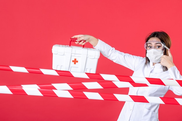 front view female doctor holding first aid kit on the red background health line covid- virus medical crime hospital danger sealed