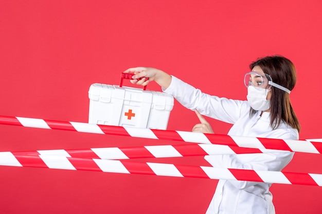 赤い床の健康ラインで応急処置キットを保持している正面図の女性医師covid-ウイルス医療犯罪病院の危険が封印されました