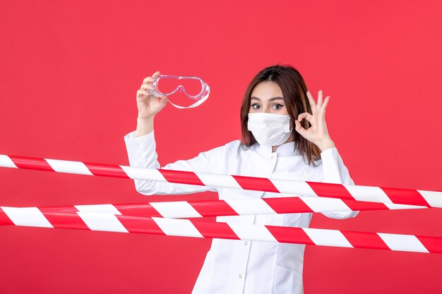 Foto vista frontale dottoressa in uniforme medica e maschera con occhiali da sole protettivi su sfondo rosso crimine linea ospedaliera virus covid sigillato