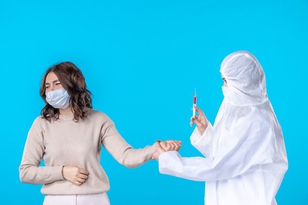 正面図青い背景のウイルス分離covid-science健康医療パンデミック病の患者のための注射を準備している女性医師