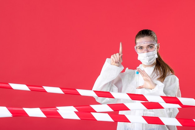 вид спереди женщина-врач в защитном костюме держит колбу на красном фоне вирус covid- здоровье вылечить больницу ткани медсестры эмоции