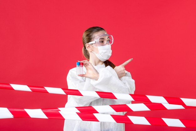 Front view female doctor in protective suit holding flasks on\
the red background covid- health cure hospital tissue nurse emotion\
virus mask