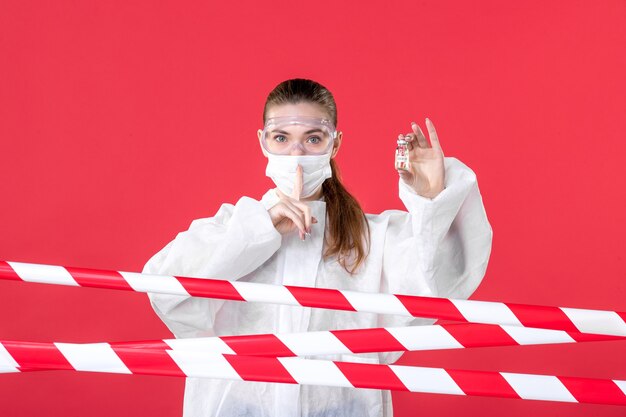 빨간색 배경 범죄 바이러스 라인 covid-병원 건강 치료 간호사에 작은 플라스크를 들고 보호복과 마스크에 전면 보기 여성 의사