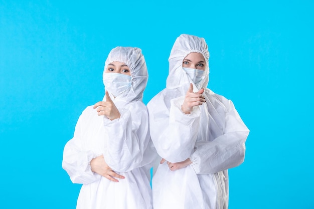 front view female doctors in protective suits and mask pointing on blue background virus pandemic hospital color health science covid-