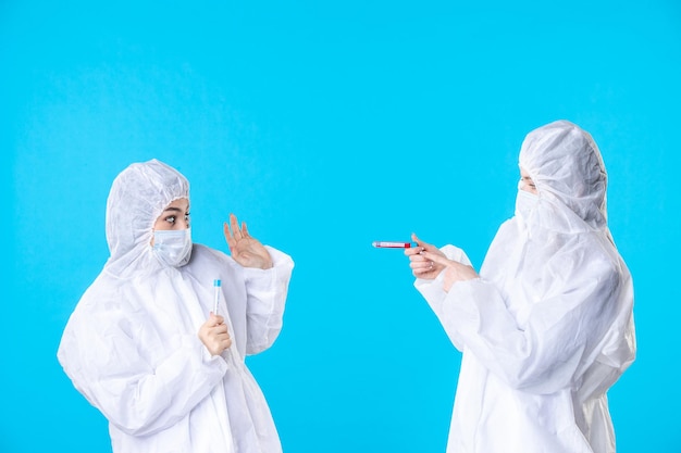 正面図青い背景のウイルス健康科学共同病院医療にフラスコを保持している防護服とマスクの女性医師