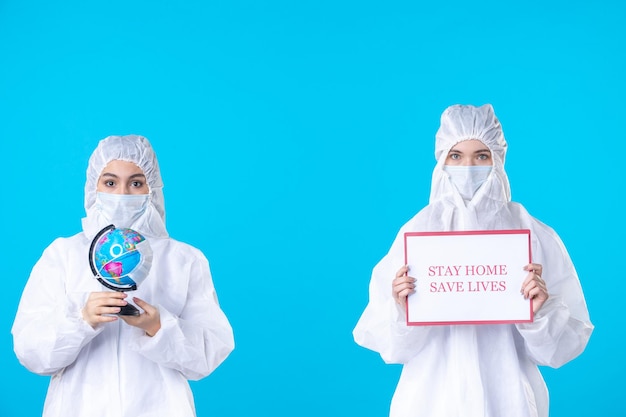 Photo front view female doctors in protective suits and masks holding stay home save lives on blue background health science covid pandemic virus medical isolation