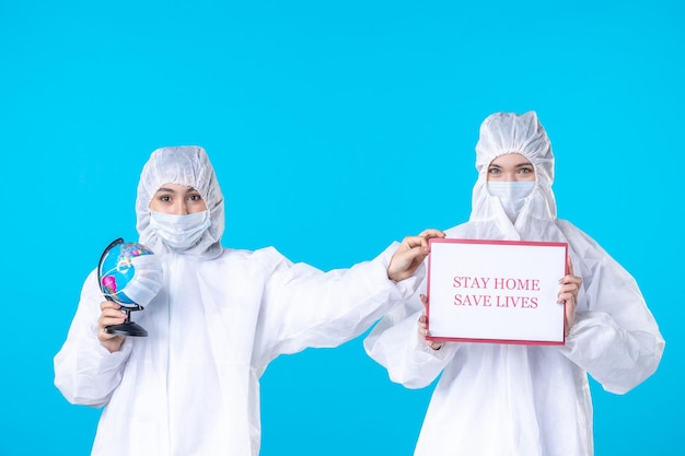 front view female doctors in protective suits and masks with warning note on the blue background virus health science covid- pandemic medical isolation