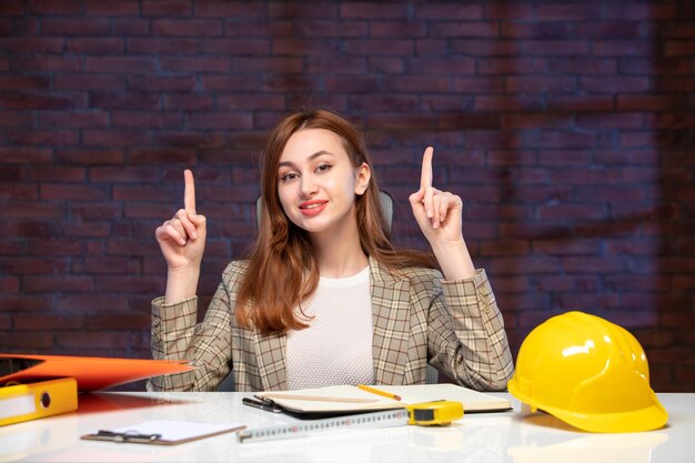 Vista frontale ingegnere donna seduta dietro il suo posto di lavoro in cantiere agenda lavoro costruttore appaltatore successo aziendale piano proprietà aziendale