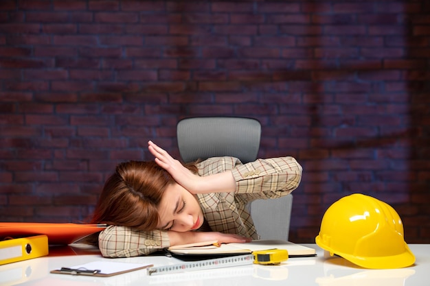 Photo front view female engineer sitting behind her working place and trying to sleep job agenda business corporate contractor success plan builder