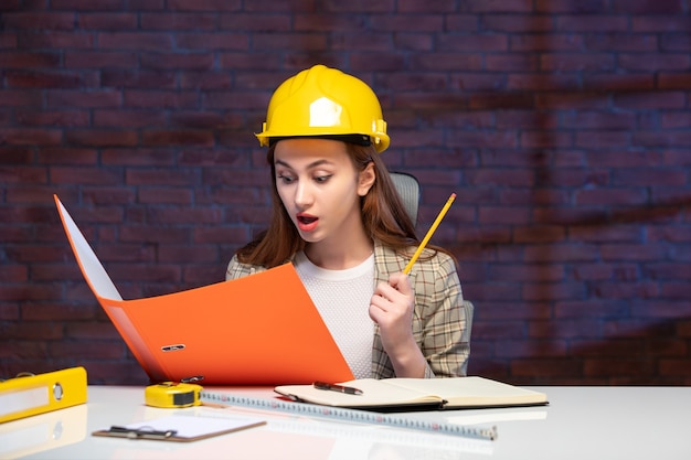 Foto vista frontale ingegnere donna seduta dietro il suo posto di lavoro che lavora con documenti lavoro successo aziendale agenda aziendale appaltatore costruttore di piani di proprietà